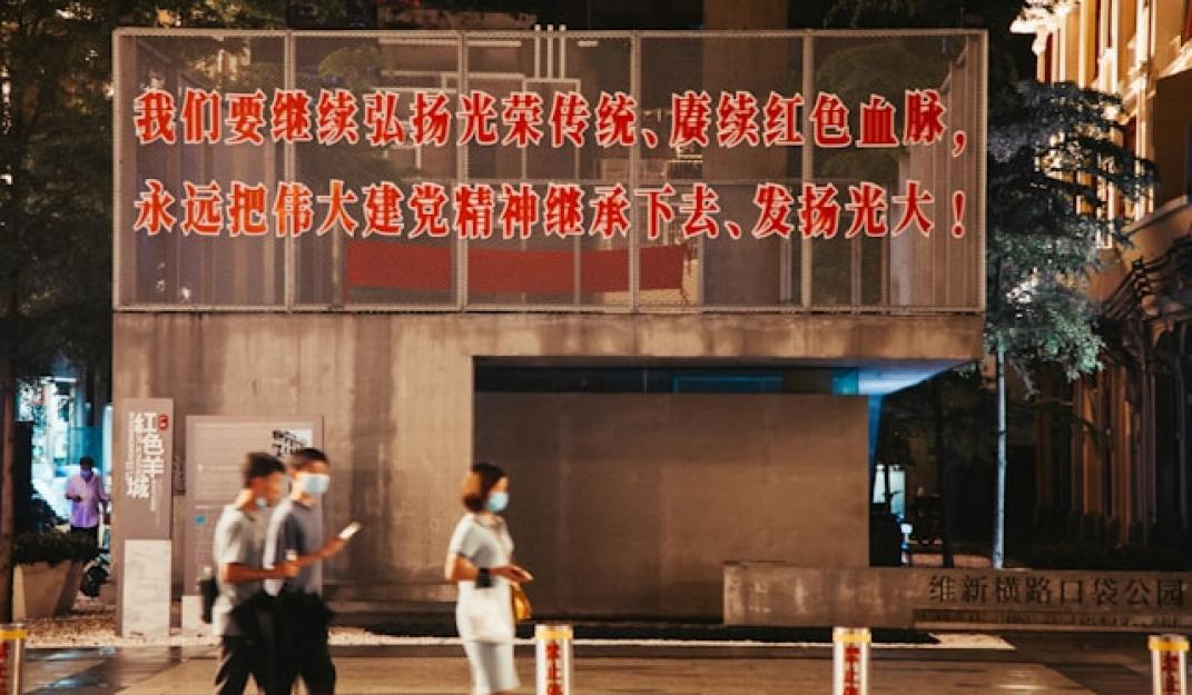 People walking on the street. Behind them there is wall with a slogan on