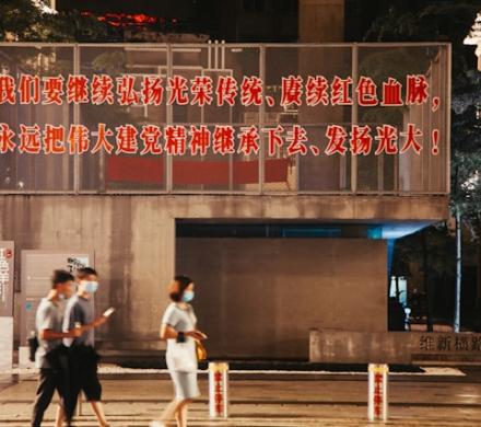 People walking on the street. Behind them there is wall with a slogan on